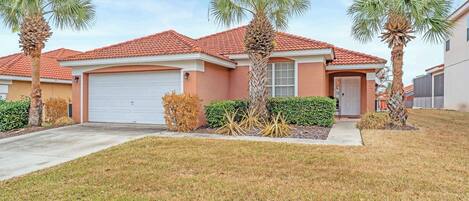 A residential house with a red-tiled roof, a garage, and a well-maintained lawn with palm trees.