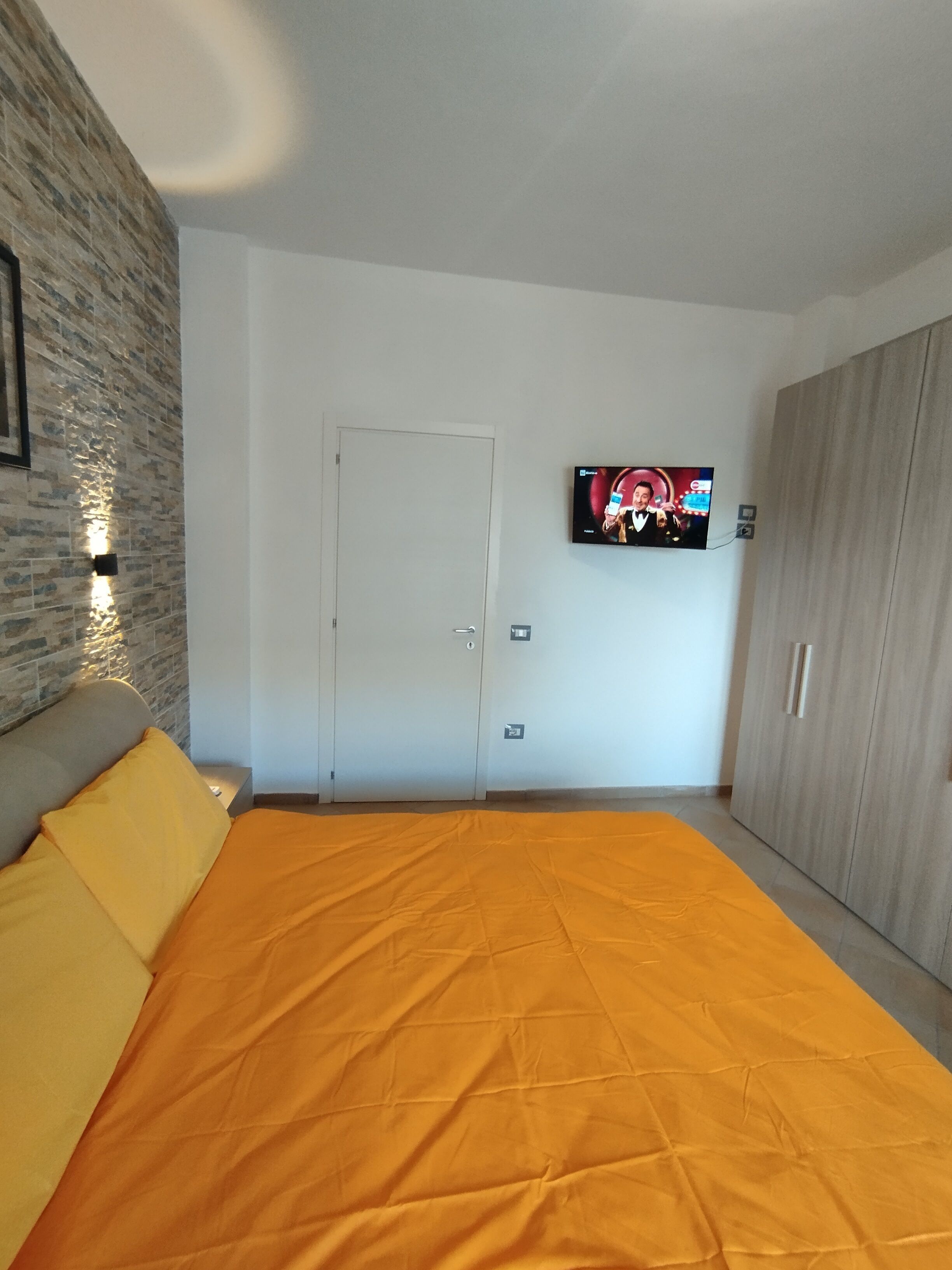 A bedroom with a large bed, a television on the wall, a wardrobe, and a door.