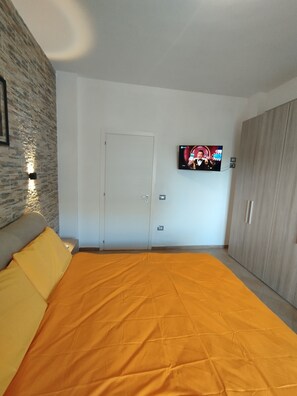 Une chambre avec un grand lit, un téléviseur fixé au mur, une armoire et une porte.
