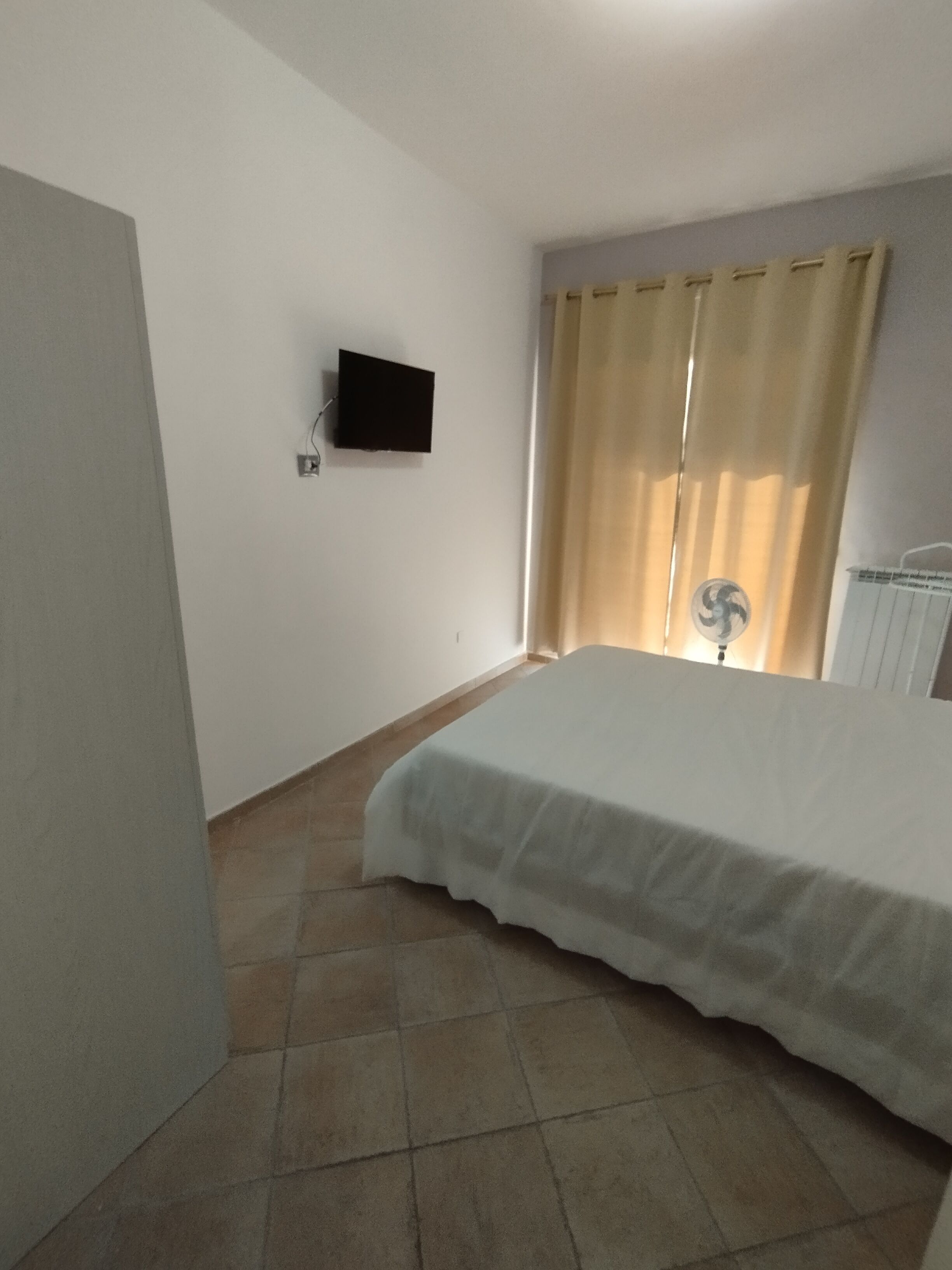 Una camera da letto con un letto, una televisione a parete e una finestra con tende.