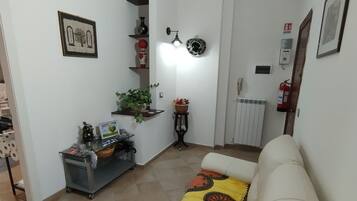 A living room with a beige sofa, a small table with decorative items, a radiator, and a wall-mounted light fixture.