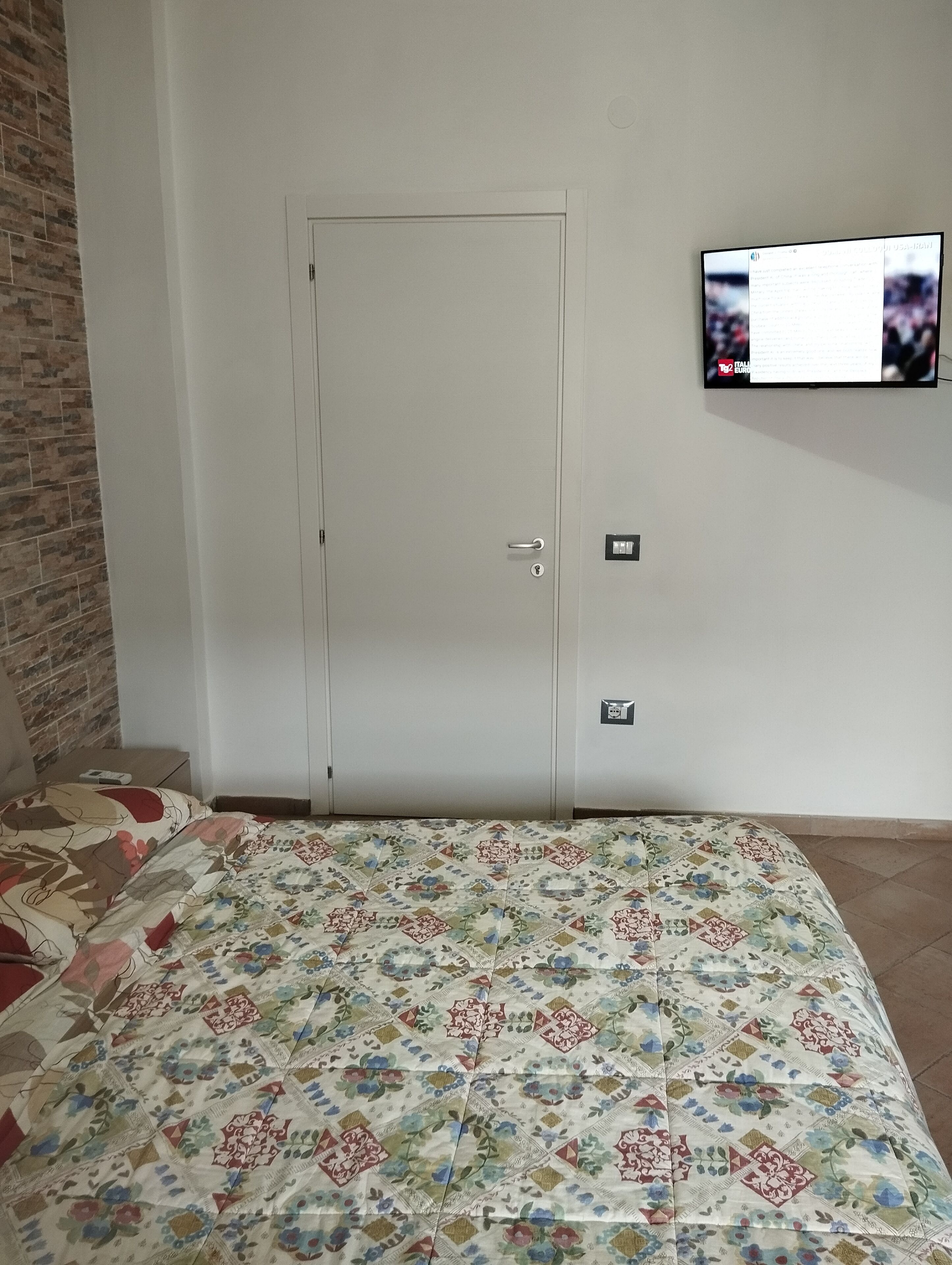 A bedroom with a bed, a television mounted on the wall, and a door with a lock.