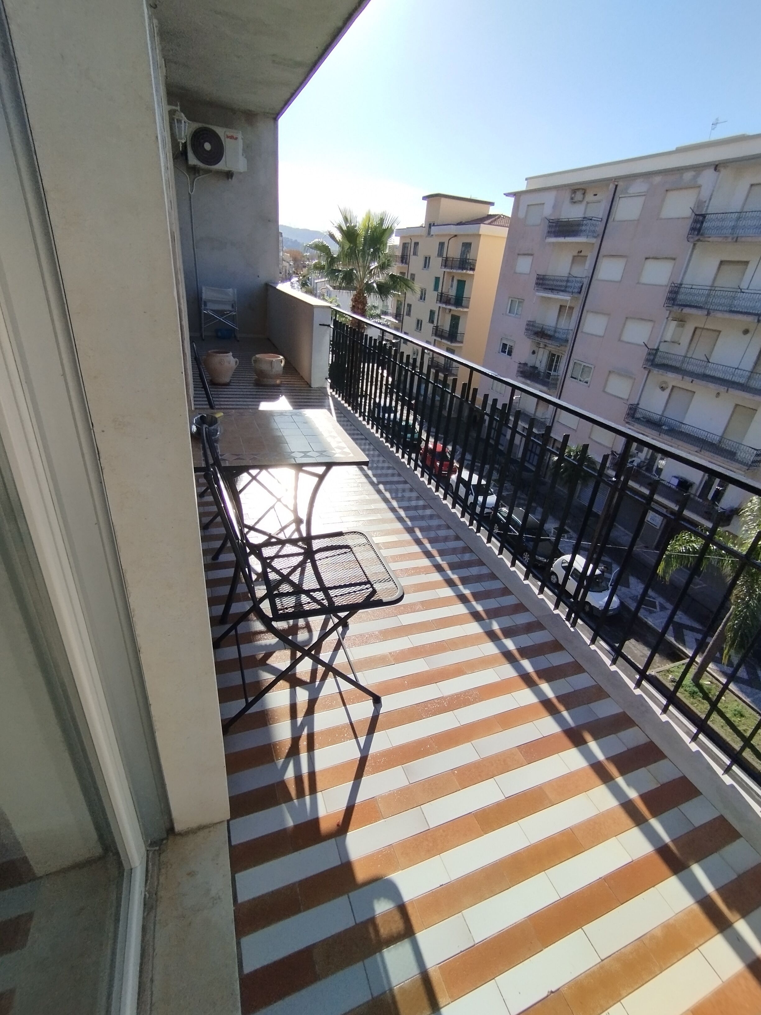 Ein Balkon mit gestreiftem Boden, einem Metalltisch und Stühlen.