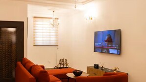 Un salon comprenant un grand ensemble de canapés, un téléviseur fixé au mur et un lustre.
