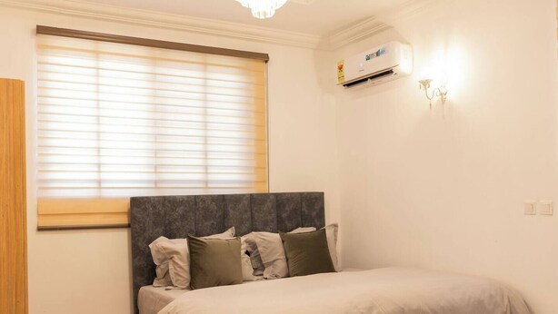 Une chambre avec un grand lit, un lustre, une fenêtre avec des stores et un appareil de climatisation.