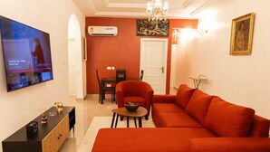 Un salon avec un canapé rouge, un téléviseur fixé au mur, une table à manger avec des chaises et un appareil de climatisation.