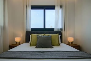 A neatly made bed with a dark headboard, two bedside lamps, and a window with curtains. - 131 LIM 201 - Stay Anna Residence Sea View Apar (Limassol)