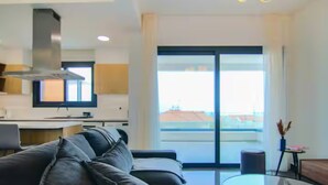 Un salón moderno con un sofá, una mesa de centro de cristal y vistas a la ciudad a través de amplios ventanales.