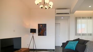 Una sala de estar moderna con un televisor de pantalla plana, una mesa de centro redonda, un sofá con un cojín azul y una araña.