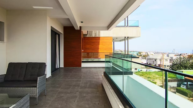 Un balcón moderno con barandilla de cristal, un sofá y vistas a la ciudad.