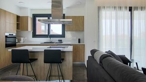 Een moderne keuken met een centraal eiland, zwarte barkrukken en een groot raam met dunne gordijnen.