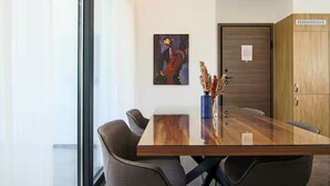 Een moderne eetruimte met een glazen tafel, stoelen, een vaas met gedroogde bloemen en een schilderij aan de muur.