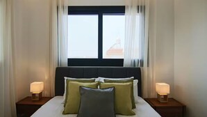 Een hotelkamer met een groot bed, twee bedlampen en een raam met dunne gordijnen.
