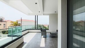 Een modern balkon met een glazen balustrade, een rieten stoel en een klein tafeltje.