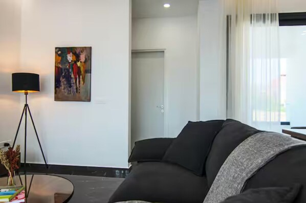 A modern living room with a black sofa, a glass coffee table, a floor lamp, and a painting on the wall. - 131 LIM 101 - Stay Anna Residence City View Apa (Limassol)
