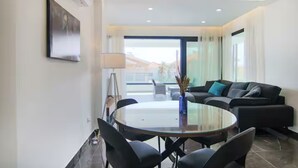 Ein modernes Wohnzimmer mit einem Glastisch, schwarzen Sofas und einem großen Fenster mit Blick auf die Stadt.