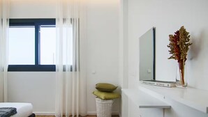 Ein modernes Schlafzimmer mit einem Bett, einem Fernseher, einem Korb mit Kissen und einer Vase mit getrockneten Blumen.