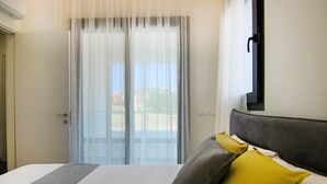 A hotel room with a bed, a window with sheer curtains, a view of the outdoors, and a mounted television on the wall. - 131 LIM 202 - Stay Anna Residence Sea View Apart (Limassol)