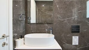 A bathroom with a marble wall, a white sink, a mirror, and a towel dispenser. - 131 LIM 202 - Stay Anna Residence Sea View Apart (Limassol)