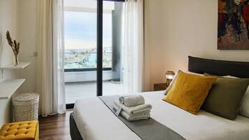Habitación de hotel con cama, una mesita, una lámpara y vista a la ciudad desde la ventana.