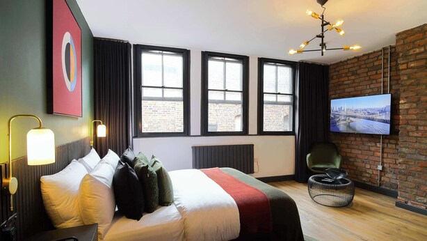 A modern hotel room with a large bed, a TV, and a brick wall. - Stay Awhile - Boutique Studio Northern Quarter (Manchester)