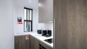 A compact kitchen with a built-in oven, a coffee maker, and a small window with blinds. - Stay Awhile - Boutique Studio Northern Quarter (Manchester)