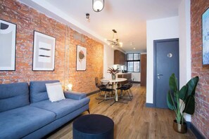 A modern living room with a blue sofa, a round coffee table, and a dining area with a white table and chairs. - Stay Awhile | Stylish Industrial 2BR Duplex, NQ (Manchester)