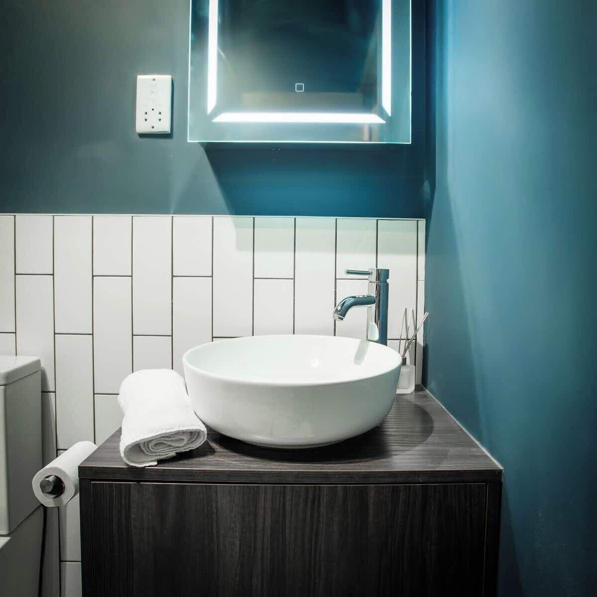 Un bagno con lavandino bianco, mobile contenitore in legno scuro e parete blu.