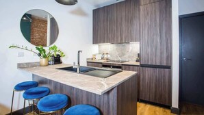 Eine moderne Küche mit Marmorarbeitsplatte, dunklen Holzschränken und einer eingebauten Spüle. Vier blaue Barhocker und ein Blumentopf stehen auf der Arbeitsfläche.