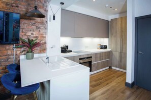 A modern kitchen with a white countertop, wooden cabinets, and a brick wall. - Stay Awhile - Luxury 2BR Duplex Northern Quarter (Manchester)