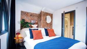 A hotel room with a brick accent wall, a bed with blue and orange bedding, a round mirror, and a potted plant. - Stay Awhile - Luxury 2BR Duplex Northern Quarter (Manchester)