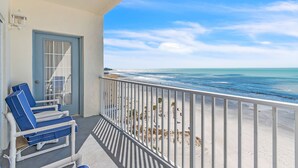 Ein Balkon mit zwei blauen Liegestühlen, einer Tür und Blick auf Strand und Meer.