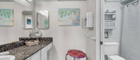 A bathroom with a white sink, vanity, and a toilet. There are two wall-mounted mirrors, a red stool, and a shower curtain.