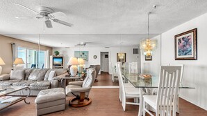 Ein modernes Wohnzimmer mit einem Glastisch, weißen Stühlen, einer Couch und einem Deckenventilator.
