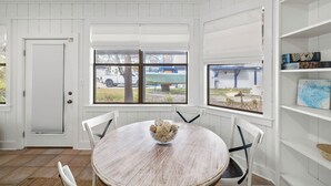 Un coin repas avec une table ronde en bois, des chaises blanches et un bol rempli d’objets décoratifs.