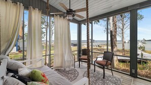 Une chambre avec un lit, un ventilateur de plafond et de grandes fenêtres donnant sur un plan d’eau.