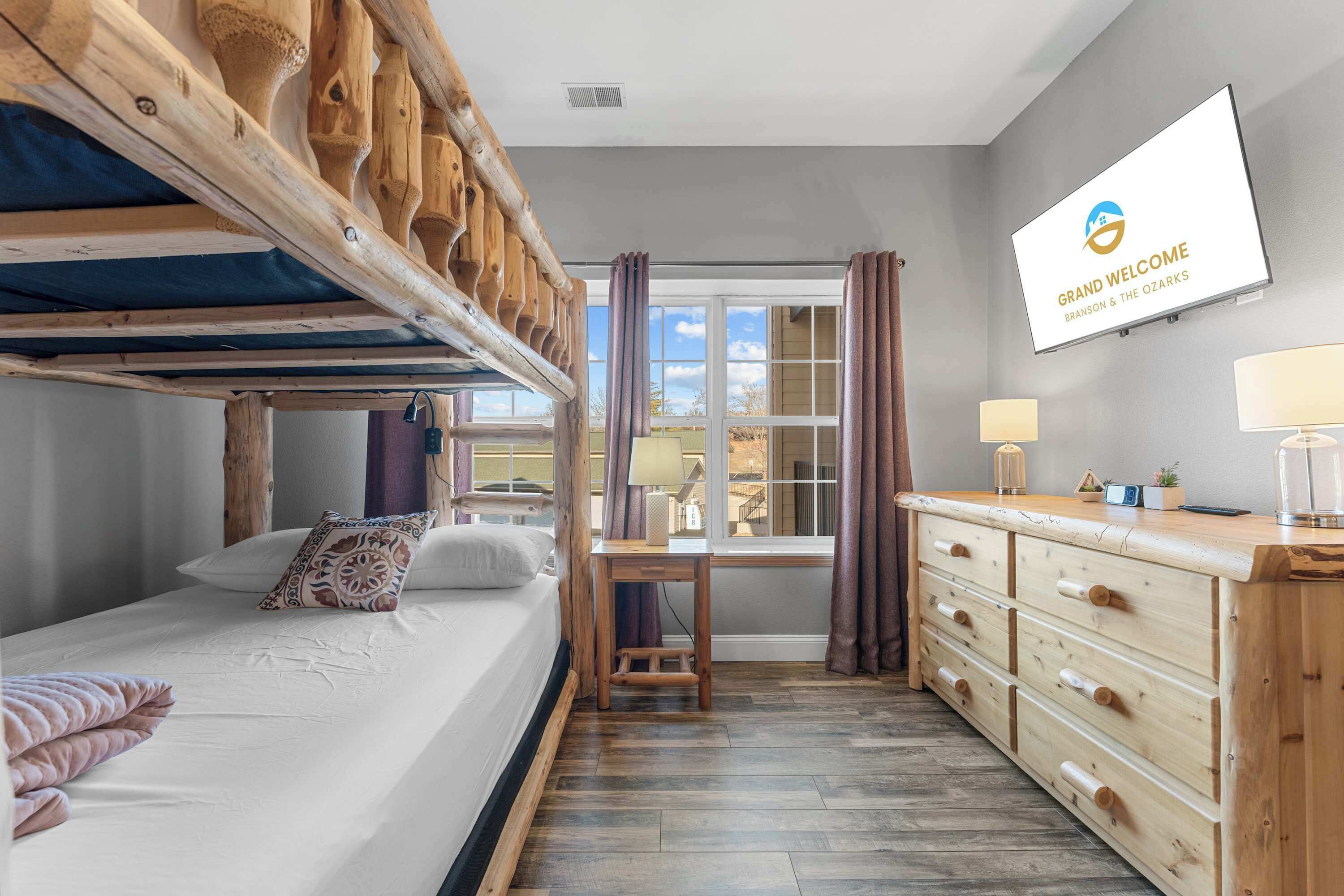 A hotel room with bunk beds, a desk, a dresser, and a TV displaying the hotel's name.