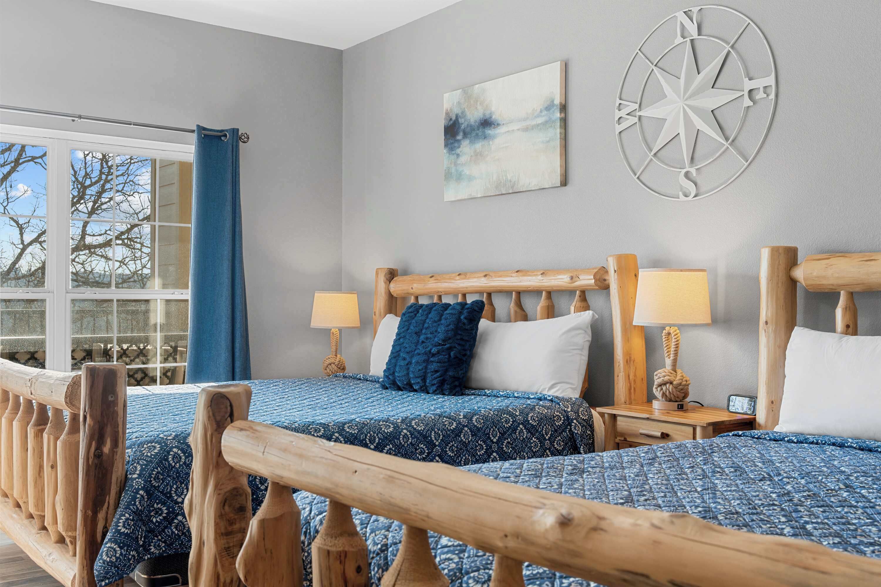 A room with two wooden beds, a compass wall decoration, and a window with a view of trees.