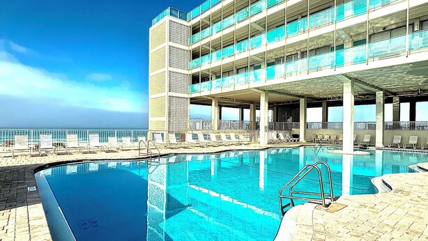 A hotel with a swimming pool, multiple balconies, and a view of the ocean. - Lovely 1 bedroom beach front studio, amazing beach access and location in PCB (Panama City Beach)