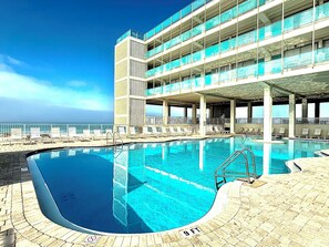 A hotel with a swimming pool, multiple balconies, and a view of the ocean. - Lovely 1 bedroom beach front studio, amazing beach access and location in PCB (Panama City Beach)
