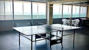 A ping pong table in a room with large windows, white chairs, and a view of the sea. - Lovely 1 bedroom beach front studio, amazing beach access and location in PCB (Panama City Beach)