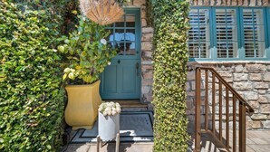 Un bâtiment en pierre avec une porte verte, un escalier en bois et une plante en pot.
