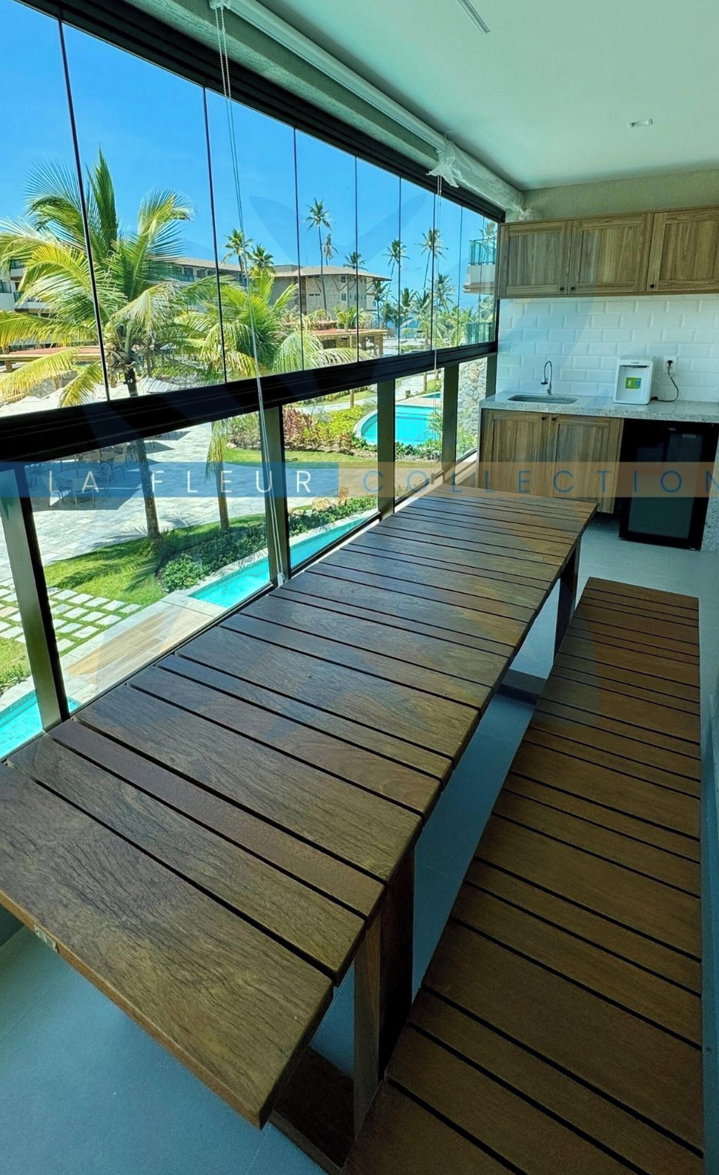 Cozinha moderna com armários de madeira e vista para uma piscina através de grandes janelas.