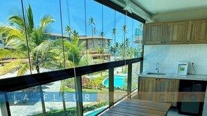 A modern kitchen with wooden cabinets and a view of a pool and palm trees. - Polinésia Villa Resort Residences LFCVH (Ipojuca)