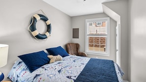 Un dormitorio con una cama, un adorno con un salvavidas, una silla y una ventana.