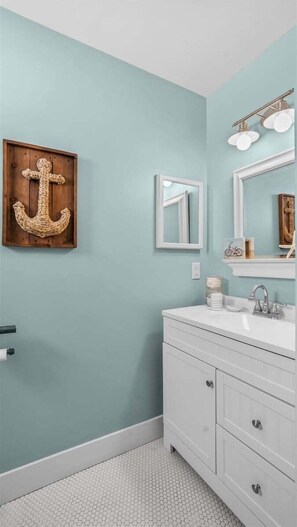 Un baño con pared azul claro, una cruz de madera, un espejo, un lavamanos y un mueble de tocador con cajones.