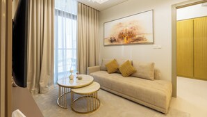 A modern living room with a sofa, two small tables, a flat-screen TV, and a large painting on the wall. - Luxury 2BR Skyline Retreat - Aykon City (Dubai)