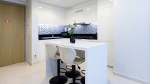 A modern kitchen with white cabinetry, a black countertop, and two bar stools. - Luxury 2BR Skyline Retreat - Aykon City (Dubai)