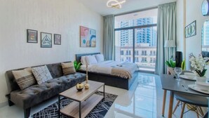 A modern hotel room with a sofa, a bed, a dining area, and a view of the cityscape. - Modern Balcony Studio in Arjan - Near Miracle Garden & Mall of the Emirates (Dubai)