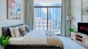 A modern hotel room with a large bed, a television, and a view of high-rise buildings. - Modern Balcony Studio in Arjan - Near Miracle Garden & Mall of the Emirates (Dubai)